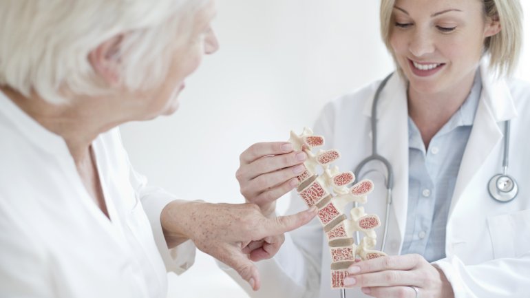 Ärztin zeigt Patient Auswirkung einer Osteochondrose der Wirbelsäule an einem Modell