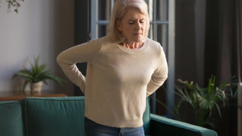 Frau merkt beim Aufstehen vom Sofa ihre Arthrose der Wirbelsäule
