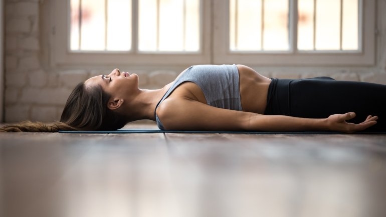 Frau liegt auf einer Yoga Matte auf dem Boden und übt progressive Muskelentspannung gegen Rückenschmerzen aus