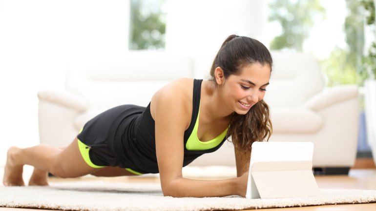 Frau macht Fitness-Übungen zuhause mit Tablet