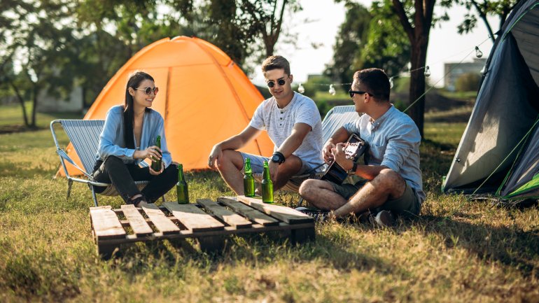 Drei Menschen sitzen zusammen zwischen Ihren Zelten und spielen Gitarre