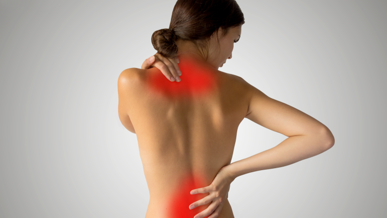 Frau mit nacktem Rücken hält sich Nacken und Rücken aufgrund von Rückenschmerzen