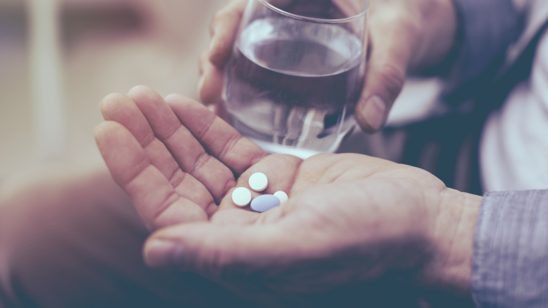 Tabletten in einer Hand und ein Glas Wasser dahinter