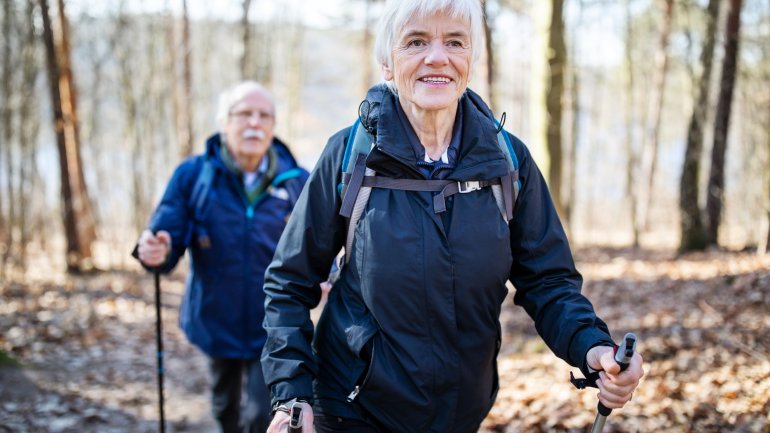 Eine ältere Frau und ein Mann gehen gemeinsam Nordic Walken im Wald