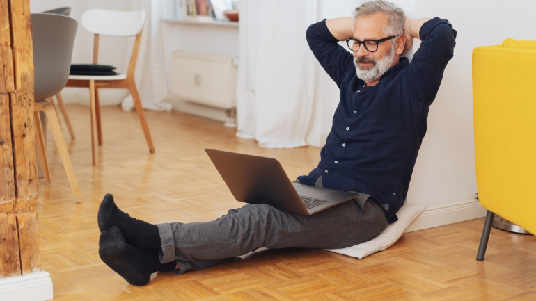 Ein Mann sitzt gegen die Wand gelehnt mit seinem Laptop auf dem Schoß auf dem Boden