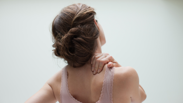 Rücken einer Frau im rosanen Top, Frau hält sich den Nacken aufgrund einer Wirbelsäulenanomalie